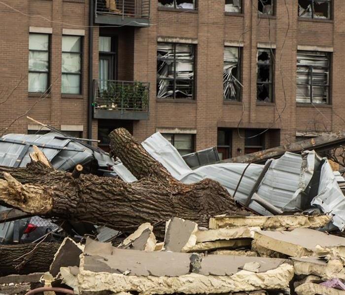 Broken tree branches, debris, and wood blocks lay scattered around the building after a tornado.   